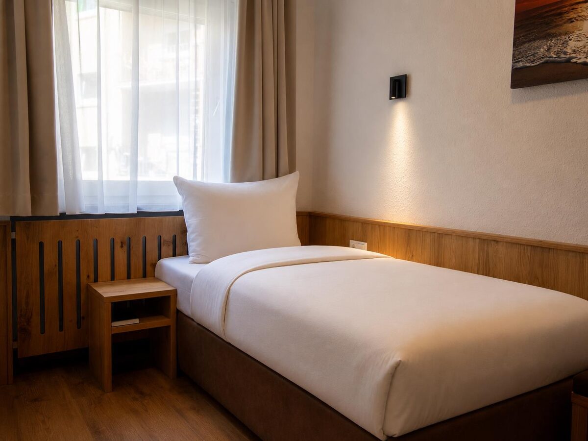 Einzelzimmer mit Bett am Fenster und Nachttisch